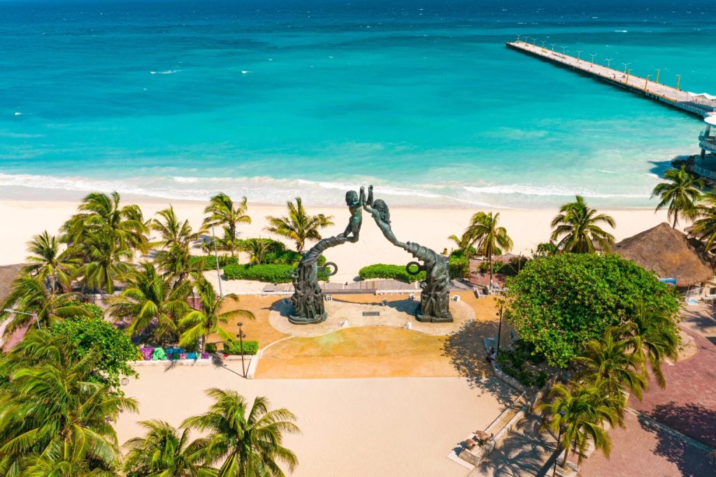 Beachfront plaza and palm trees beside the turquoise sea in Playa del Carmen.